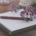 Open notebook with pink pen and delicate flowers resting on its pages