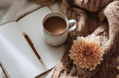 A cozy scene with a cup of coffee, open journal, pen, knitted blanket, and a flower, symbolizing calm reflection and self-care.