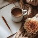 A cozy scene with a cup of coffee, open journal, pen, knitted blanket, and a flower, symbolizing calm reflection and self-care.